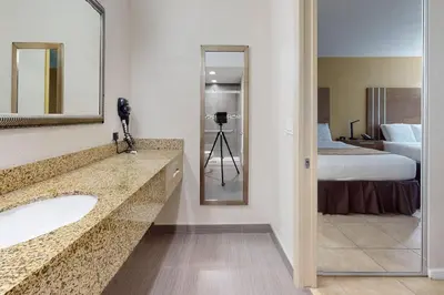 a bathroom with a sink and a mirror and a bed at Rodeway Inn & Suites Fort Lauderdale Airport & Cruise Port in Fort Lauderdale