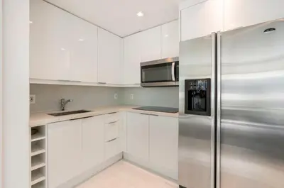 a kitchen with white cabinets and a stainless steel refrigerator at Beachfront Bentley Hotel One Bedroom Suite with Balcony and Beach access in Miami Beach