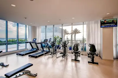 a gym with treadmills and ellipticals in a room with windows at Bluebird Suites Monte Carlo Miami Beach in Miami Beach