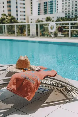 a hat and a towel next to a swimming pool at Iberostar Waves Berkeley Shore in Miami Beach