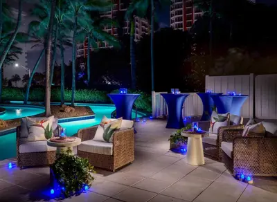 a patio with chairs and tables and a pool at night at Pelican Grand Beach Resort, a Noble House Resort in Fort Lauderdale