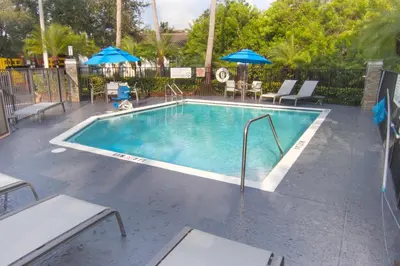 a swimming pool with chairs and umbrellas on a patio at Holiday Inn Express and Suites Fort Lauderdale Airport West by IHG in Davie