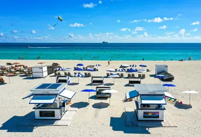 a beach with chairs and umbrellas and the ocean at The Sagamore Hotel South Beach in Miami Beach