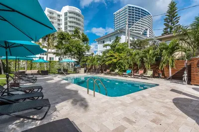 a swimming pool with chairs and trees and buildings at Nobleton Hotel in Fort Lauderdale