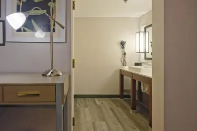 a bathroom with a sink and a desk with a lamp at The Palms Inn & Suites Miami, Kendall, FL in Kendall