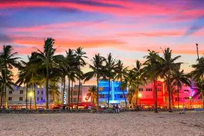 a beach with palm trees and buildings at sunset at Barbizon on Ocean Drive Apartments in Miami Beach
