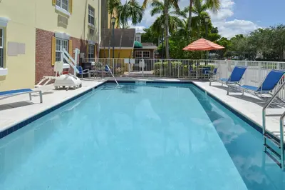 a large blue swimming pool with chairs and an umbrella at Candlewood Suites Miami Lakes by IHG in Miami Lakes