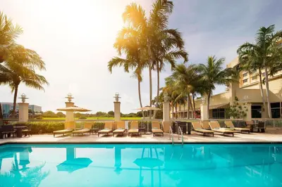 a pool with chairs and palm trees and a building at Renaissance Fort Lauderdale West Hotel in Plantation