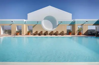a large swimming pool with chairs and a building at Sheraton Suites Fort Lauderdale West in Plantation