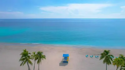 a blue truck on a beach with palm trees and the ocean at CH Luxury Condos & Studios On The Beach in Hollywood