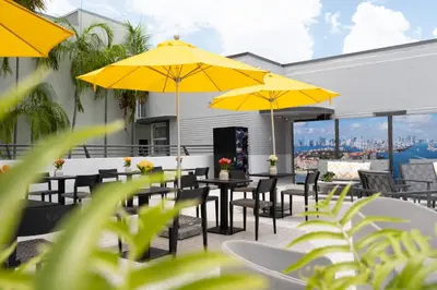 a patio with tables and chairs with yellow umbrellas at The Cove By Renzzi in Miami Beach