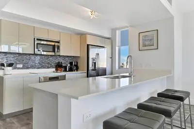 a kitchen with white cabinets and a counter with stools at Three-Bedroom Beachwalk Resort Apartment in Hallandale Beach