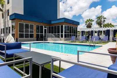 a swimming pool with blue chairs and a building at Hampton Inn & Suites Miami Airport South/Blue Lagoon in Miami
