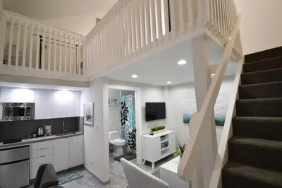 a living room with a staircase and a kitchen at Loft wqueen bed steps to Hollywood Beach in Hollywood