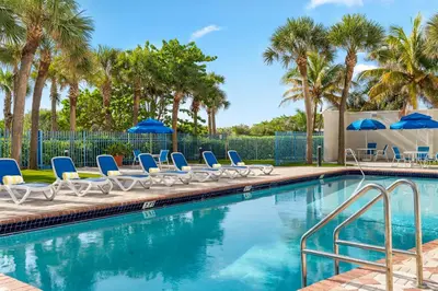 a pool with chairs and umbrellas and palm trees at Crystal Beach Suites Miami Oceanfront Hotel in Miami Beach