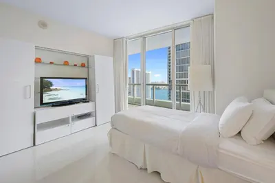 a white bedroom with a large bed and a television at ICON Brickell residences in Miami