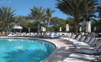 a pool with chairs and umbrellas and palm trees at One Bal Harbour Ritz Bal Harbour in Miami Beach
