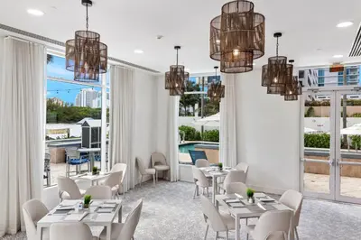 a restaurant with white tables and chairs and large windows at GALLERY One - A DoubleTree Suites by Hilton Hotel in Fort Lauderdale