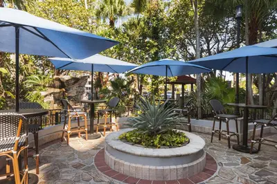 a patio with tables and chairs with blue umbrellas at Embassy Suites by Hilton Fort Lauderdale 17th Street in Fort Lauderdale