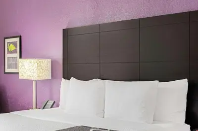 a bedroom with a bed with white pillows and purple walls at La Quinta by Wyndham Miami Lakes in Miami Lakes