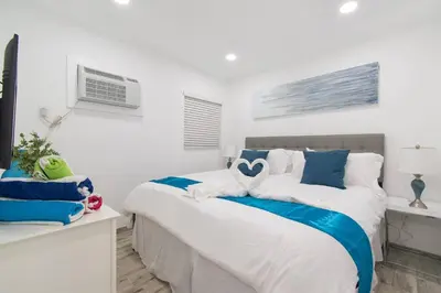a white bedroom with a bed with blue and white pillows at Renovated studio wocean view boardwalk steps in Hollywood