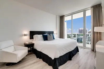 a bedroom with a bed and a chair and a large window at City View Balcony steps from Restaurants, Peacock Park & Marina in Miami