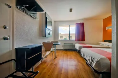 a room with two beds and a desk and a table at Motel 6-Fort Lauderdale, FL in Fort Lauderdale