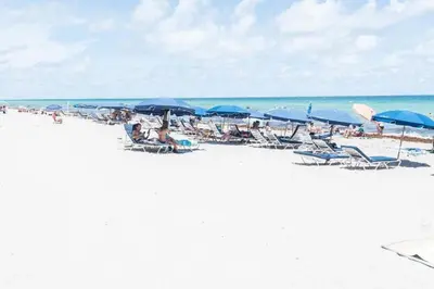 a group of people sitting on a beach with umbrellas at Hallandale Beach Intracoastal View Apartments in Hollywood