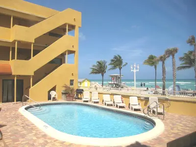 a swimming pool in front of a hotel with chairs and the ocean at Hollywood Sands Resort in Hollywood
