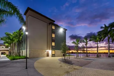 a building with palm trees in front of a sunset at WoodSpring Suites Miramar in Miramar