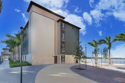 a building with palm trees next to a body of water at WoodSpring Suites Miramar in Miramar
