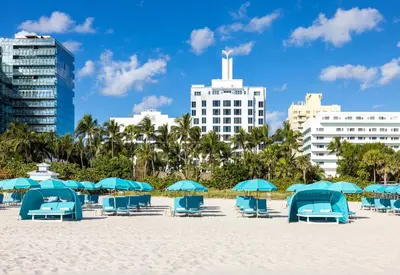 a beach with blue chairs and umbrellas and buildings at The Palms Hotel & Spa in Miami Beach