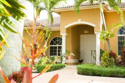 a yellow house with a white door and palm trees at Yuli's Home in Miami