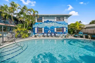 a swimming pool in front of a building with a house at Blue Bell Apartment Hotel in Fort Lauderdale