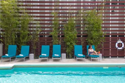 a woman sitting in chairs next to a swimming pool at Dorchester Hotel & Suites in Miami Beach
