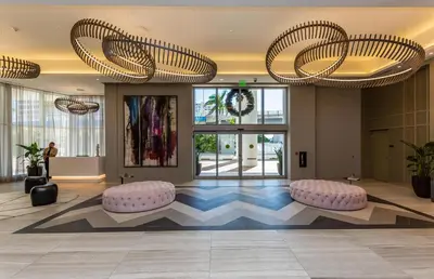 a lobby with two large chandeliers and pink ottomans at Espectacular Condo Esquina Beach House Hollywood Apartamento in Hollywood
