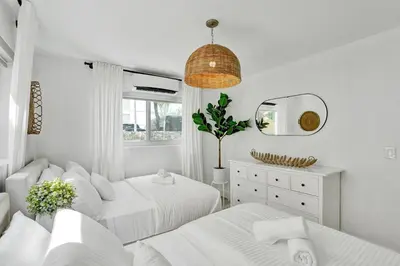 a white bedroom with two beds and a mirror at Lincoln Villa Suites in Miami Beach