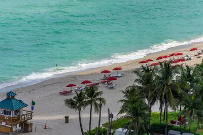 a beach with red umbrellas and people on the beach at Trump International Beach Resort Ocean View 1100 sf 1 Bed 1Bth Privately Owned Sunny Isles in Miami Beach