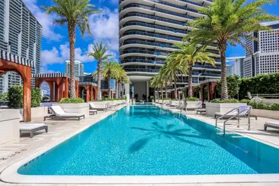 a swimming pool with palm trees and a building at Aluna Lux Suites at SLS Lux Brickell Building in Miami