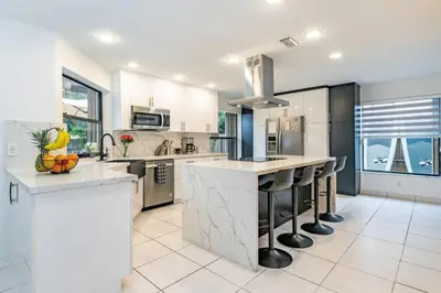 a white kitchen with a large island with bar stools at Lux House Heated Spa & Free Boat Tour! in Fort Lauderdale