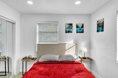 a white bedroom with a red bed with two tables at 2 Bdrm Modern House Mins From Beach & Casino Hb1 in Hallandale Beach