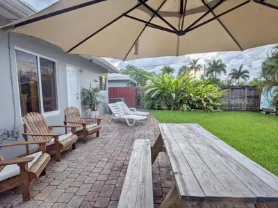 a patio with wooden benches and an umbrella at Surf House - Paddleboards - Canoes -1 mile to Wilton Manors in Fort Lauderdale