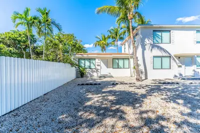 a house with a white fence and palm trees at Renovated Apts with Kitchen, Fast WiFi, Smart TV, Roku & Pool Onsite 4 mi to Surfside Beach in North Miami