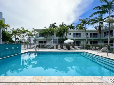 a swimming pool in front of a building with palm trees at Tranquilo in Fort Lauderdale