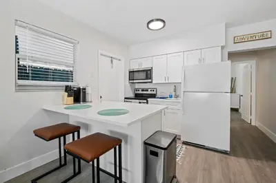 a white kitchen with a refrigerator and two bar stools at Comfy BNB w/ King Bed + Work/Travel + Beach 8 Min in Hallandale Beach
