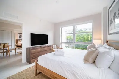 a white bedroom with a large bed and a flat screen tv at Tucker at Palmer Dadeland Miami in Miami