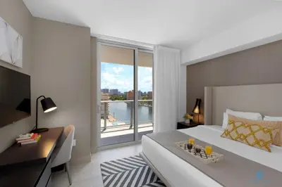 a bedroom with a bed and a desk and a large window at Wrap Around Balcony, Paradise Beach & Amazing Pools in Hollywood