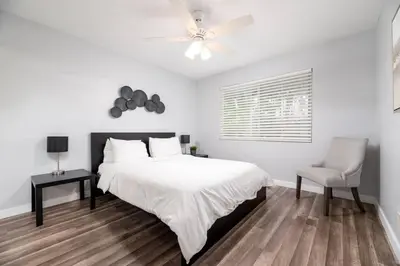 a white bedroom with a bed and a chair at The Palms at Middle River Terrace 1 in Fort Lauderdale