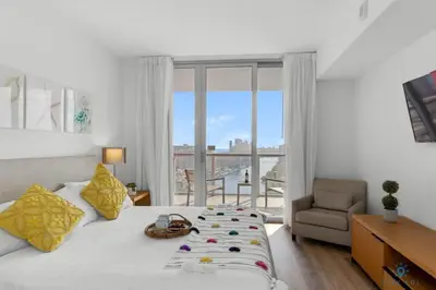 a bedroom with a bed and a chair and a window at Infinite View with Balcony, Pool, Gym plus Near Beach in Hallandale Beach