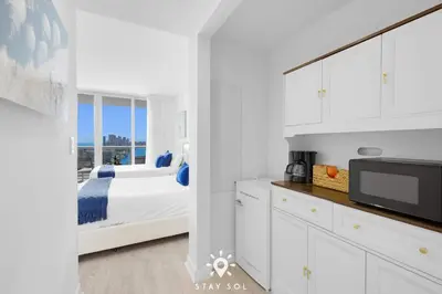 a white bedroom with a bed and a tv at Infinite View - Balcony - Pool - Gym - Near Beach in Hallandale Beach